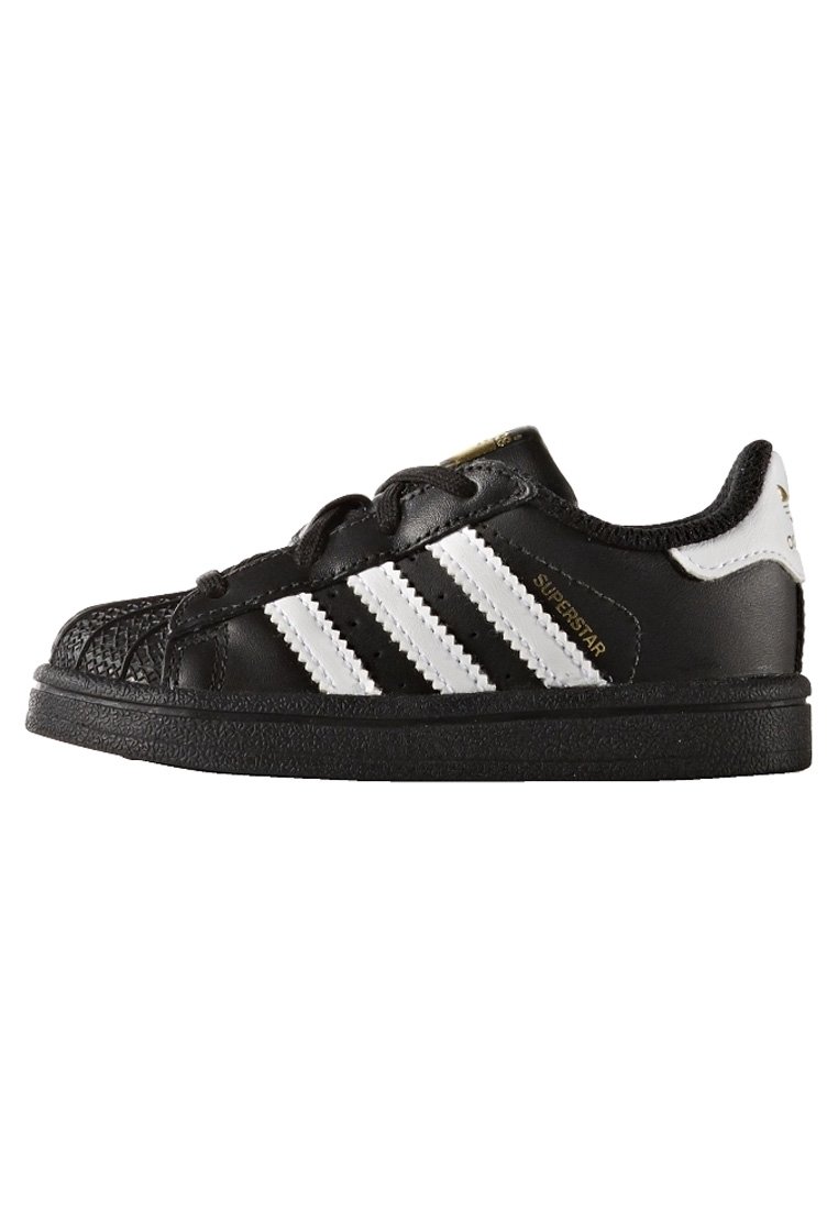Svart Adidas Superstar-sneaker med vita ränder, skaldopp, och guld "Superstar"-text på sidan, sedd från yttersidan.
