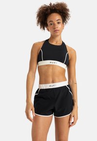 Zwarte sportieve crop top met wit Roxy-logo en accenten. Gecombineerd met zwarte shorts met een witte tailleband en bijpassende afwerking.