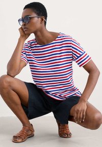 Striped t-shirt with red, blue, and white stripes, paired with black shorts and brown strappy sandals, showcasing a relaxed fit and crew neckline.