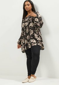 Blusa nera a fiori con maniche lunghe e vita arricciata, abbinata a jeans skinny neri e scarpe beige slip-on. Presenta una vestibilità ampia.