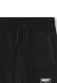 Pantalons de jogging noirs avec taille élastique, cordon de serrage ajustable, poches latérales et patch logo DKNY sur la poche inférieure. Texture de tissu lisse.