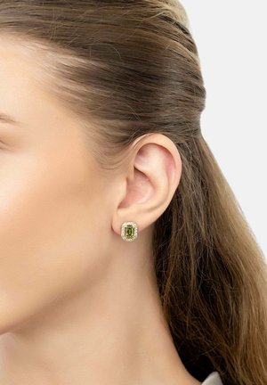 Orecchio sinistro di donna con orecchino a perno rettangolare con pietra verde circondata da piccole pietre trasparenti e montatura in oro.