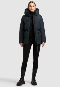 Puffer jacket in dark blue, featuring a hood, zipper front, and side pockets. Worn with black leggings and lace-up black boots.