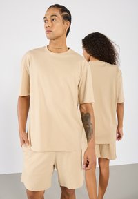 Beige pamut póló rövid ujjakkal, lazább szabással és kerek nyakkivágással, amelyhez illeszkedő sortot visel, sima textúrával és laza dizájnnal.