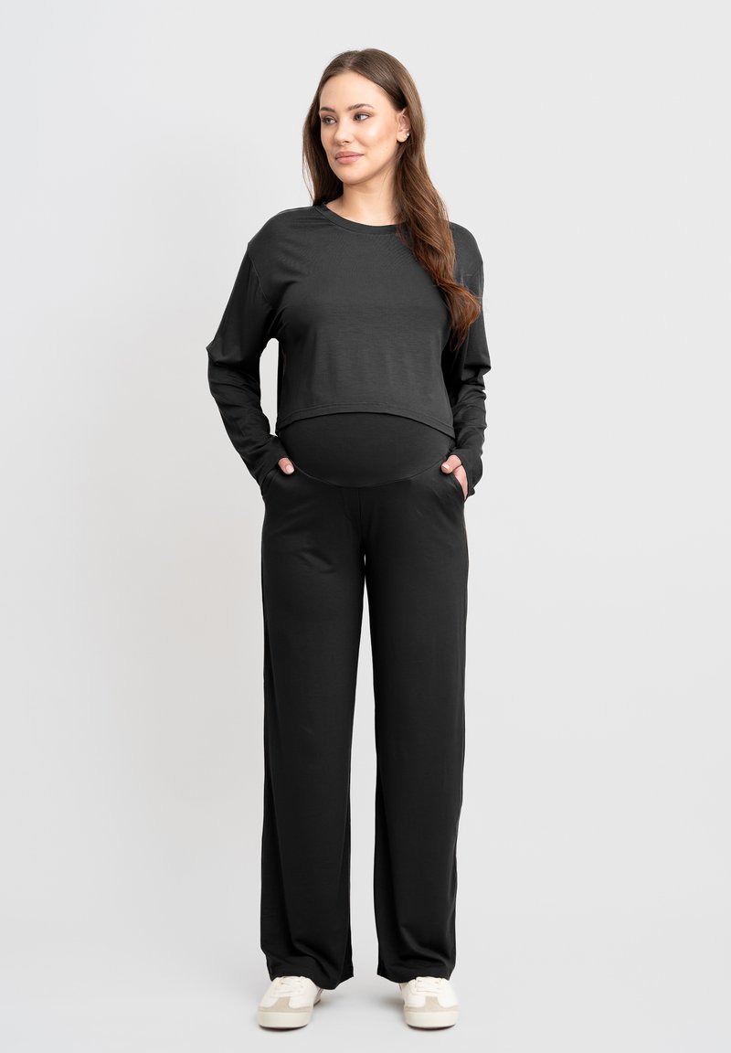 Schwarzes, langärmliges, cropped Top mit rundem Halsausschnitt, kombiniert mit schwarzen, weiten Hosen. Beide aus glattem, elastischem Stoff mit seitlichen Taschen gefertigt.