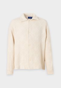 Beige gombos ing, texturált anyagból készült, gyémántmintával és klasszikus gallérral. Négy gomb az elején.
