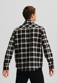 Camisa de franela de cuadros en blanco y negro con un ajuste relajado, puños abotonados y un cuello clásico. Textura suave con un dobladillo ligeramente deshilachado.