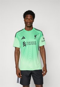 Zelený brankársky dres s čiernymi doplnkami, s okrúhlym výstrihom, prúžkovanými ramenami a logami sponzorov, navrhnutý s prechodovým vzorom.