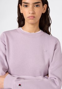 Felpa viola chiaro realizzata in misto cotone, con scollatura a costine e logo ricamato su petto e manica. Tessuto morbido, design casual.