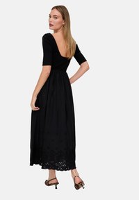 Schwarzes Maxikleid mit figurbetontem Oberteil, kurzen Ärmeln und tief ausgeschnittenem Rückenausschnitt. Der Rock ist mit bestickten Akzenten am Saum versehen.