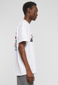 Hvit bomull T-skjorte med korte ermer, med multicolor grafiske design og striper på ryggen. Rett passform med rund hals.