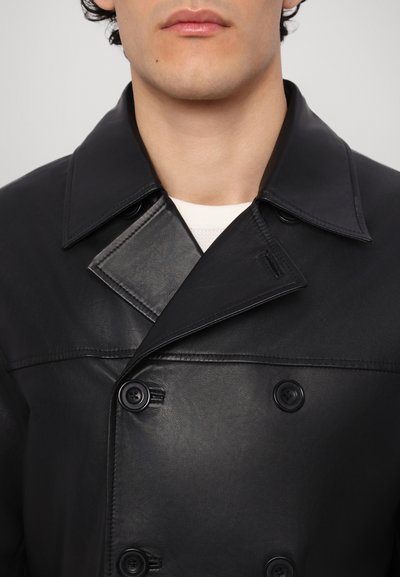 Manteau croisé en cuir noir avec grands revers, dotée de deux boutons, texture lisse et design ajusté. Aucun motif ou accent visible.