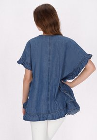 top in denim con maniche corte a volant, vestibilità rilassata e orlo sfrangiato. Il retro presenta una cucitura centrale ed è realizzato in tessuto denim blu.