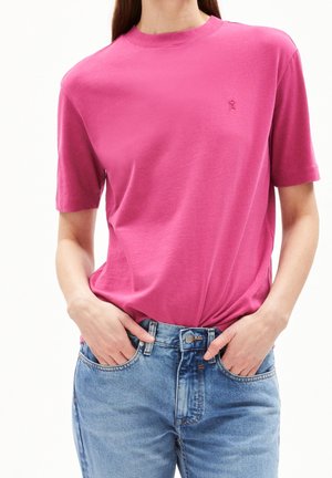 Fuchsia T-shirt met korte mouwen en een ronde hals, gemaakt van zacht katoen. Een klein logo is op de borst gedrukt. Gecombineerd met blauwe jeans.