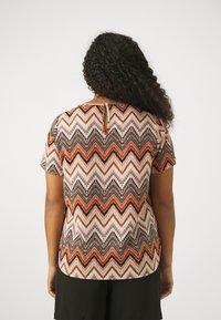 Top à manches courtes avec un motif zigzag multicolore dans des nuances d'orange, de rouge et de noir, avec un détail dos en clef. Tissu léger.
