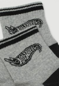 Šedé ponožky s černými pruhy na vršku a charakteristickým černým logem. Měkká textilie s pohodlným střihem.