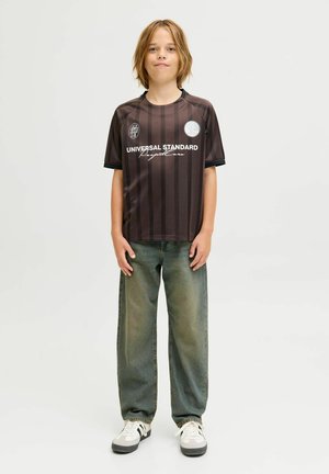 Jersey de manga corta a rayas en negro y marrón con el texto "UNIVERSAL STANDARD", combinado con unos vaqueros ligeros de corte ancho en azul claro y zapatillas blancas.