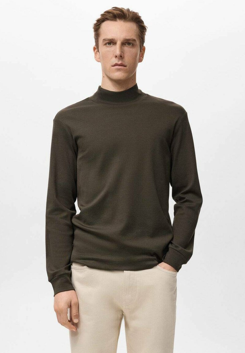 Dunkelolivgrünes, langärmeliges Rollkragenshirt aus weichem Stoff, mit lockerem Schnitt und minimalistischem Design, kombiniert mit hellbeigen Hosen.