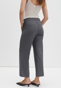 Grijze, wijduitlopende broek met een losse pasvorm, elastische tailleband, twee zijzakken en een gladde textuur. Gecombineerd met zwarte instapschoenen.