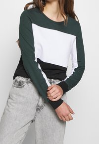 Långärmad sweatshirt med mörkgröna, vita och svarta färgblock. Tillverkad av mjukt tyg med rund halsringning och kontrasterande muddar.