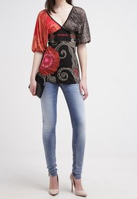 Top multicolor con base negra y patrones de paisley, mangas en rojo y gris. Combinado con jeans ajustados de un azul claro y tacones nude.