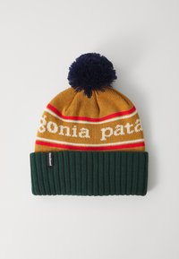 Gorro de malha com pom-pom azul-marinho, listras amarelo mostarda e vermelhas, texto branco e rótulo de punho canelado verde escuro em fundo branco.