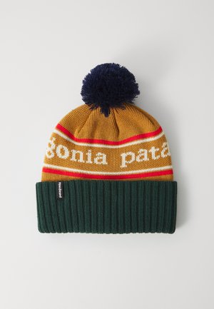 Kötött sapka tengerészkék pom-pommal, mustársárga és piros csíkokkal, fehér szöveggel, és sötétzöld bordázott mandzsettával fehér háttéren.