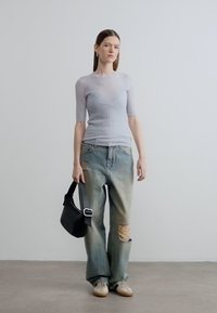 Ανοιχτό γκρι ριμπ κοντομάνικη μπλούζα, φθαρμένο μπλε τζιν με ανοιχτό πλύσιμο, μαύρη τσάντα χειρός και μπεζ αθλητικά παπούτσια με υφασμένες σόλες.