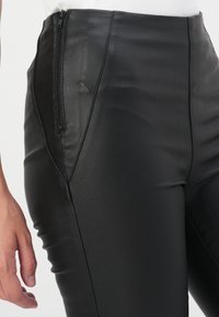 Pantaloni in pelle nera a vita alta con una texture liscia. Presentano una zip laterale e cuciture sartoriali per una silhouette aderente.