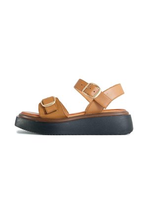 Tan leather platform sandal with two adjustable gold buckles and thick black sole, side view on white background.