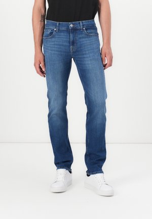 Light blue denim jeans with a straight cut, five-pocket design, button closure, and subtle fade. Paired with white sneakers.