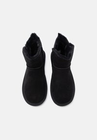 Czarne zamszowe botki za kostkę z miękkim, puszystym wykończeniem. Posiadają okrągły czubek oraz przeszycia wokół górnej części i podeszwy.