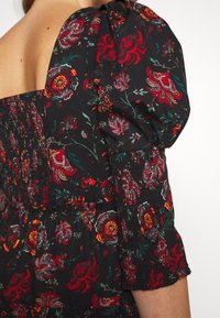 Gros plan d'une robe en tissu noir, motifs floraux rouges et orange, avec une manche bouffante sur l'épaule et le haut du bras d'une personne.