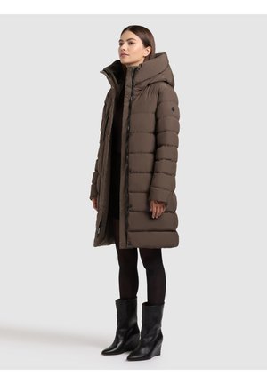 Brun dunjakke med høj krave, med knaplukning foran og ribbet tekstur. Bæres med knæhøje sorte støvler og et mørkt outfit.