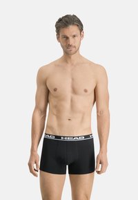 Boxers noirs en coton avec une ceinture blanche à logo. Le design présente une coupe ajustée et un style minimaliste sans motifs.