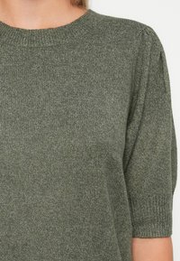 Haut en tricot vert à manches courtes avec un col rond, présentant un tissu texturé et des manches légèrement bouffantes.