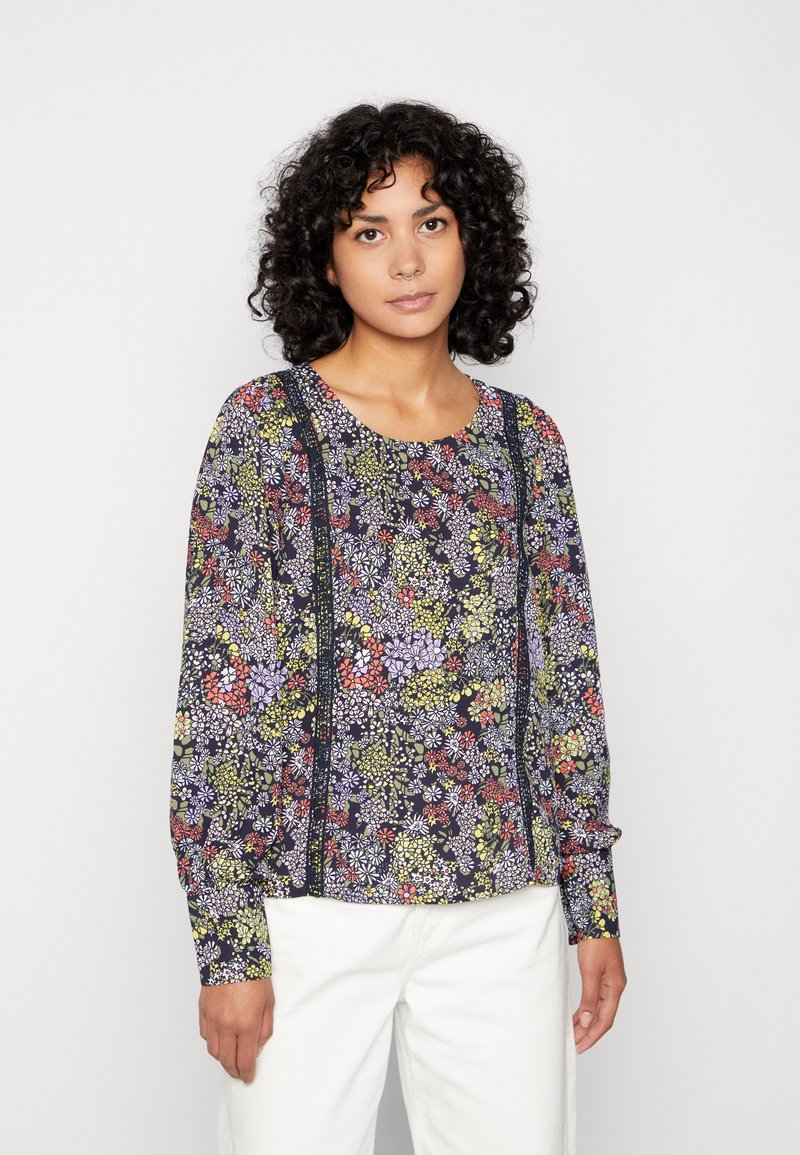 Blusa de manga longa com flores, apresentando um fundo escuro com flores roxas, verdes e vermelhas, complementada por realces verticais escuros.