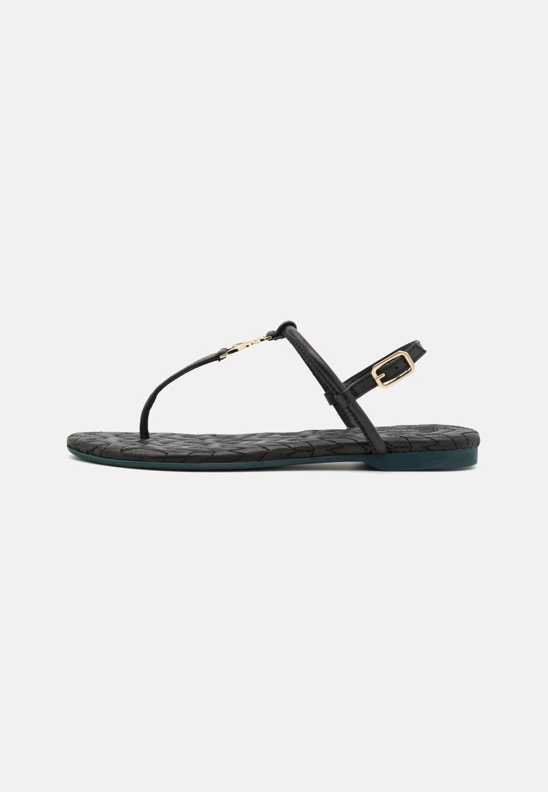Sorte flate sandaler med vevet tekstur, tanga-stil stropp, justerbar ankelspenne og en mørkegrønn såle. Gulldetaljer.