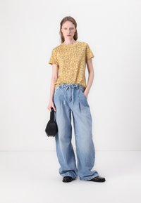 Yellow patterned t-shirt with short sleeves, paired with light blue high-waisted wide-leg jeans. Accessories include a black handbag and flat shoes.