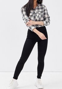 Leggings noirs taille haute associés à une chemise à carreaux noir et blanc avec boutons, manches longues et deux poches poitrine.