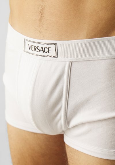 Boxer-briefs en coton blanc avec une taille élastique ribbed blanche, ornée d'un logo "VERSACE" noir brodé sur une étiquette rectangulaire.