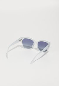 Ochelari de soare supradimensionați, cu lentile gri închis cu gradient; rame transparente și brațe subțiri cu un branding subtil pe lateral.