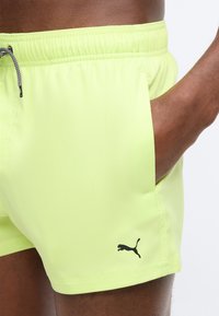 Άνδρας που φοράει ανοιχτό πράσινο σορτς Puma με ελαστική μέση και κορδόνι, χέρι στην πλαϊνή τσέπη, εμφανές λογότυπο Puma στο πόδι.