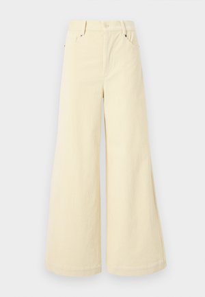 Calças largas feitas de um tecido bege suave com um acabamento texturizado, apresentando bolsos frontais, passantes para cinto e um fecho de botão único.