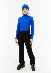 Plava dugosleeve osnovna majica s polu-zipom, uparen s crnim skijaškim hlačama i crnim skijaškim čizmama. Odijelo je prilagođeno za zimske sportove.