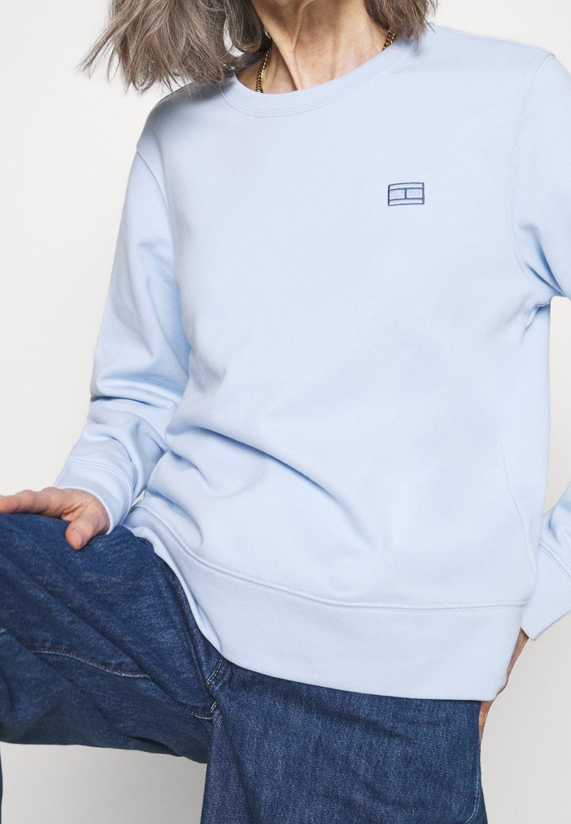 Sudadera de corte crewneck en azul claro, fabricada con un tejido suave, que presenta un pequeño logo bordado en el pecho y puños y dobladillo acanalados.