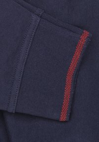 Marineblauwe stof met een gladde textuur. Voorzien van een rode stikaccent langs de rand. Zichtbare naadlijnen benadrukken het gestructureerde ontwerp.