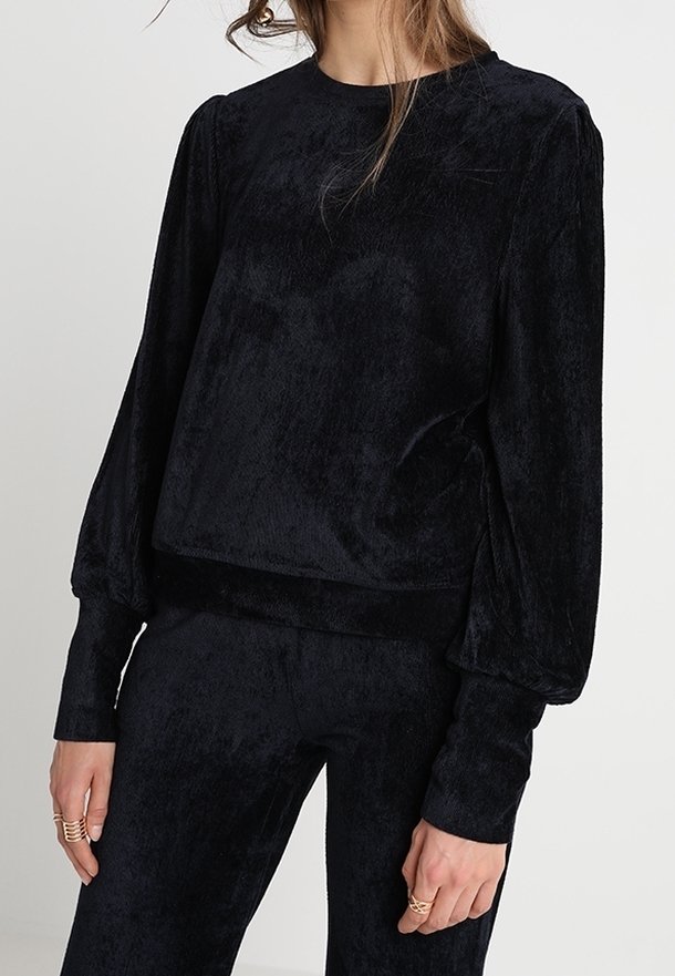 Svart plyschpullover med långa, vida ärmar, rund halsringning och en mjuk, texturerad yta. Tight vid midjan för en kortad silhuett.