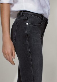 Mustat denimit, joissa on slim-fit-leikkaus, klassinen viiden taskun muotoilu ja hillitty sauman yksityiskohtaus. Silkkinen pinta, kapea lahkeensuu.