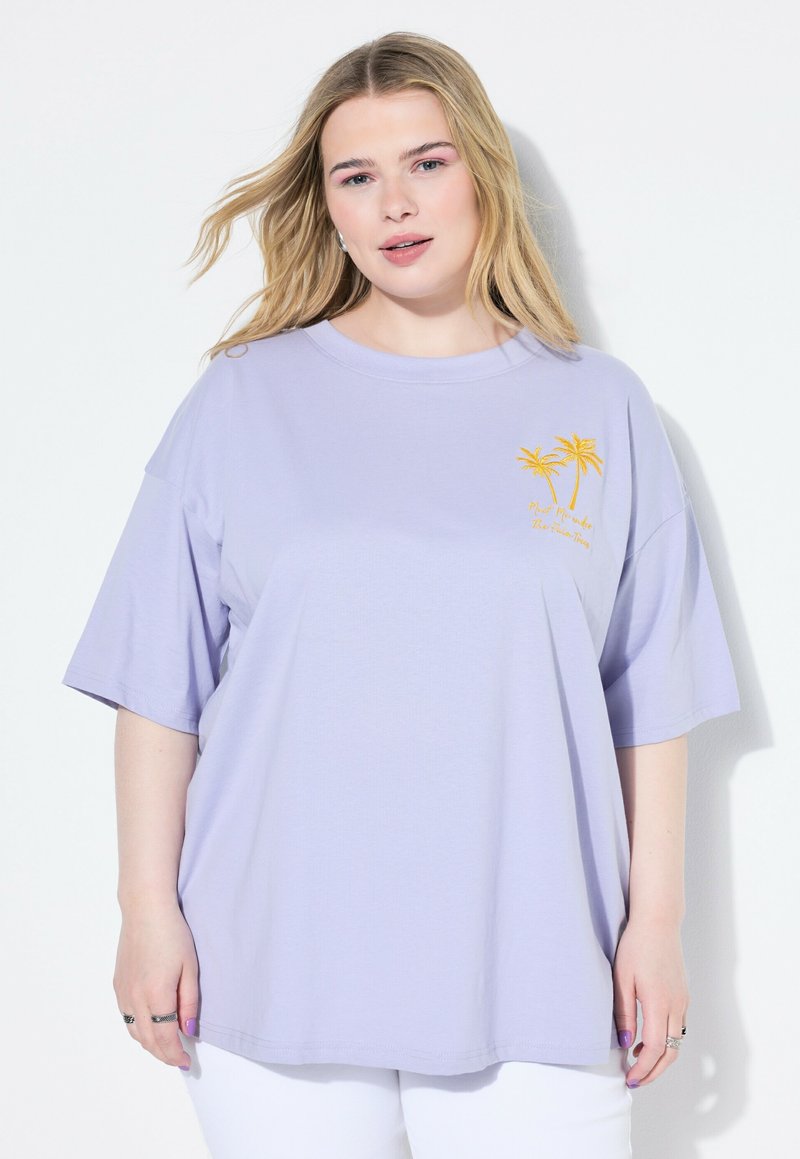 T-shirt oversize lavande en tissu doux, avec des manches courtes et un motif sur la poitrine représentant deux palmiers jaunes accompagnés de texte.